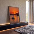 Veleiro navegando no mar laranja ao pôr do sol com farol aceso no penhasco, quadro decorativo