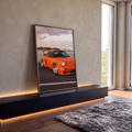 Quadro Decorativo Carro Clássico Laranja Pôr do Sol no Mar | quadros decorativos para sala | carro esportivo laranja com aerofólio à beira da água e skyline ao fundo | em Quadros para Sala | Porao dos Quadros