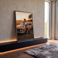 Mulher de boné e botas apoiada em muscle car enferrujado ao pôr do sol no campo, quadro decorativo