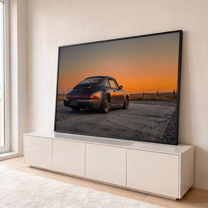 Porsche 911 cinza visto de trás sob céu laranja do pôr do sol em campo seco, quadro decorativo