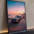 Mustang clássico preto e carros antigos em estrada litorânea ao pôr do sol rosa e laranja, quadro decorativo