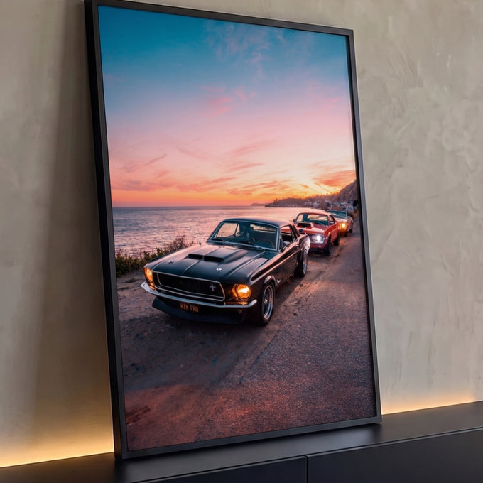 Mustang clássico preto e carros antigos em estrada litorânea ao pôr do sol rosa e laranja, quadro decorativo