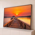 Píer de madeira com quiosque sobre lago calmo sob céu laranja de pôr do sol, quadro decorativo