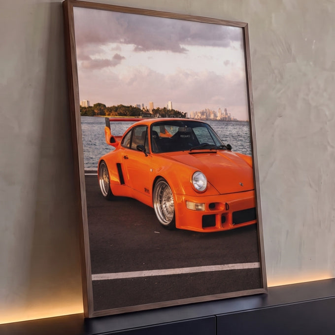 Quadro Decorativo Carro Clássico Laranja Pôr do Sol no Mar | quadros decorativos para sala | carro esportivo laranja com aerofólio à beira da água e skyline ao fundo | Porao dos Quadros