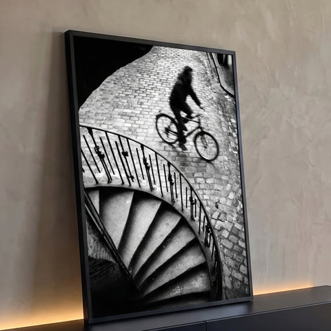 Ciclista desfocado em rua de paralelepípedos e escada em caracol, em preto e branco, quadro decorativo