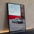 Porsche 911 retrô cinza estacionado em pátio com muro vermelho e prédio de tijolos, quadro decorativo
