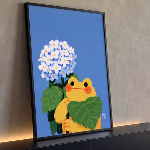 Sapinho amarelo fofo segurando folha verde ao lado de hortênsias brancas em fundo azul, quadro decorativo