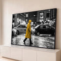 Pessoa de capa amarela atravessando rua chuvosa com táxis em cena preto e branco, quadro decorativo
