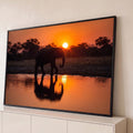Elefante em silhueta caminhando à beira do lago com reflexo ao pôr do sol laranja, quadro decorativo