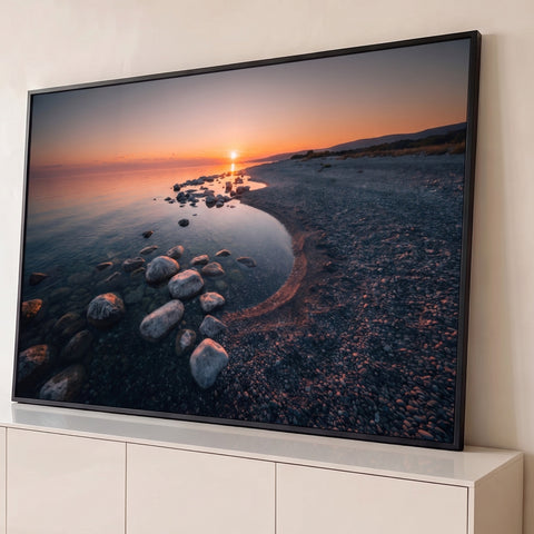 Pôr do sol sobre mar calmo com pedras na água cristalina e praia de seixos, quadro decorativo