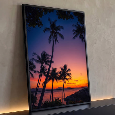 Coqueiros em silhueta ao pôr do sol tropical, céu laranja e lilás sobre o mar e rochas, quadro decorativo