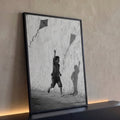 Menino descalço correndo com pipa e sombra projetada em parede rachada, preto e branco, quadro decorativo