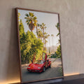 Carro esportivo vermelho anos 80 com portas abertas entre palmeiras e cidade ao fundo, quadro decorativo