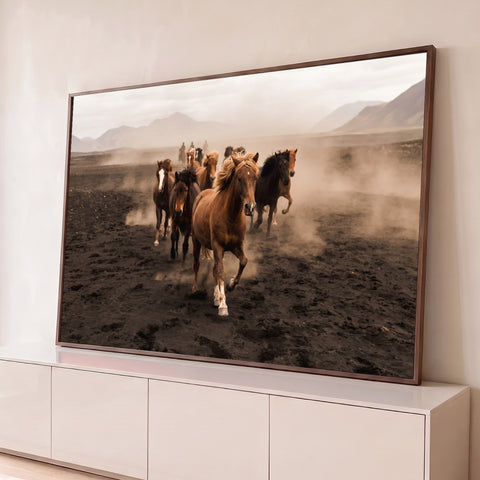 Manada de cavalos galopando na areia vulcânica escura com poeira e montanhas ao fundo, quadro decorativo