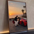 Casal abraçado ao lado de Ferrari vermelha ao pôr do sol com palmeiras e mar, quadro decorativo