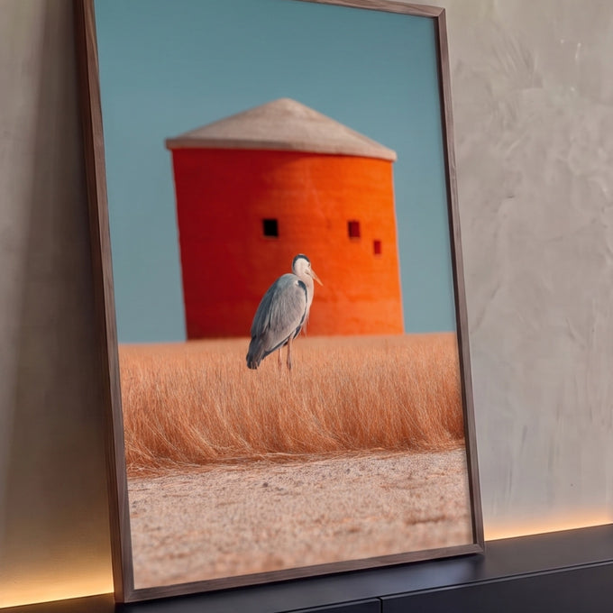 Garça-cinzenta em campo de grama dourada com silo laranja e céu azul ao fundo, quadro decorativo
