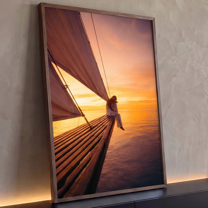 Mulher sentada na proa de veleiro sobre o mar ao pôr do sol em tons laranja, quadro decorativo
