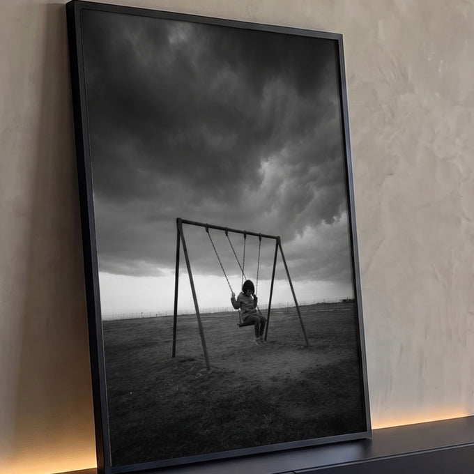 Criança sozinha em balanço num campo sob nuvens de tempestade, fotografia preto e branco, quadro decorativo