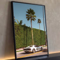 Carro esportivo branco estacionado sob palmeiras altas, muro verde e céu azul, quadro decorativo