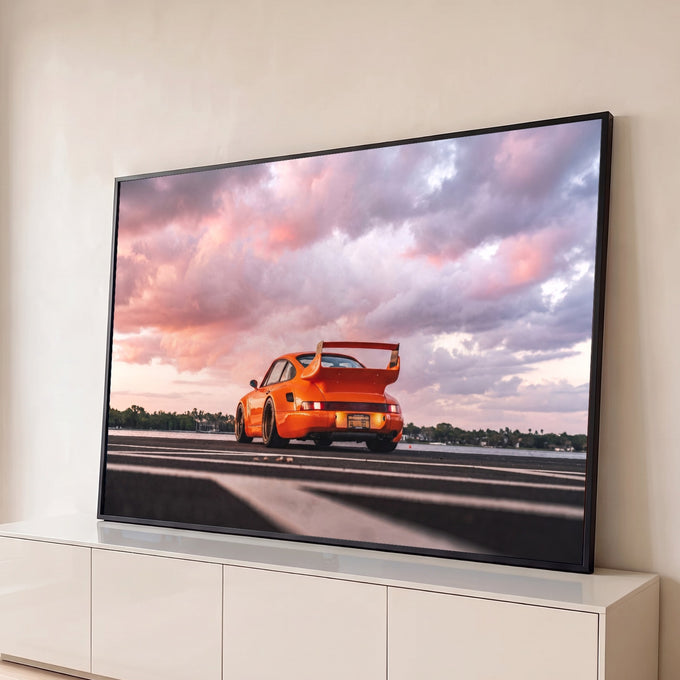Porsche 911 laranja widebody com aerofólio sob céu de nuvens rosa ao pôr do sol, quadro decorativo