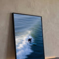 Surfista de roupa preta em prancha azul sobre onda do mar com espuma branca e movimento, quadro decorativo