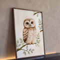 Corujinha marrom em aquarela pousada em galho com folhas verde-sálvia sobre fundo creme, quadro decorativo