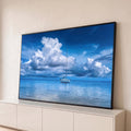 Veleiro branco ancorado em mar azul calmo sob grandes nuvens brancas e céu azul profundo, quadro decorativo