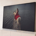 Mulher de vestido vermelho montada em cavalo branco sobre píer de pedra em lago escuro, quadro decorativo
