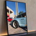 Porsche 911 clássico azul claro com rodas esportivas, carro vermelho e obelisco ao fundo, quadro decorativo