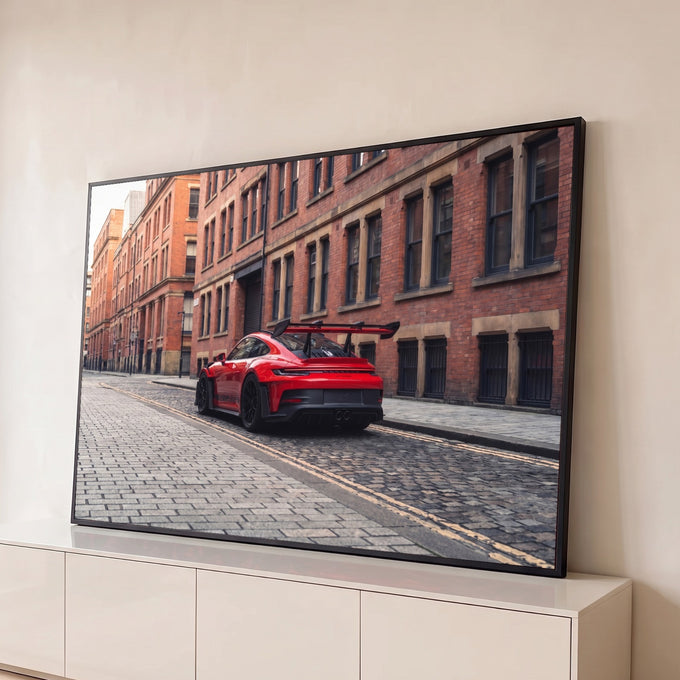 Porsche 911 GT3 RS vermelho com aerofólio em rua de pedras entre prédios de tijolo, quadro decorativo
