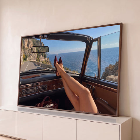 Pernas com scarpin vinho no painel de conversível clássico, estrada costeira e mar azul, quadro decorativo