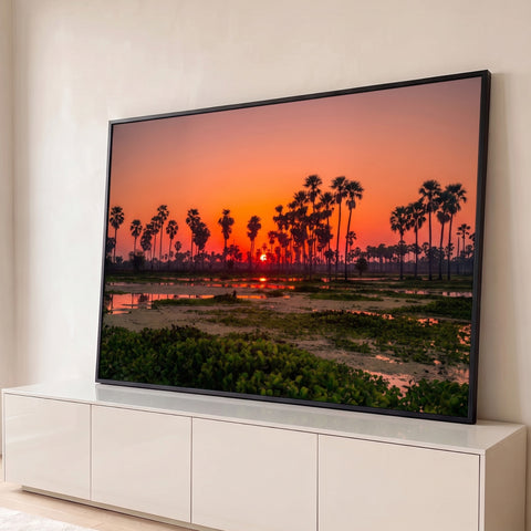 Pôr do sol laranja entre palmeiras em silhueta refletido em lagoa com plantas aquáticas, quadro decorativo