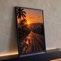 Pôr do sol laranja sobre rodovia com palmeiras, moto e cidade entre montanhas, quadro decorativo