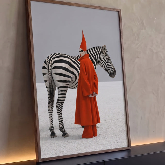 Mulher de casaco vermelho, chapéu pontudo e máscara ao lado de zebra em deserto branco, quadro decorativo