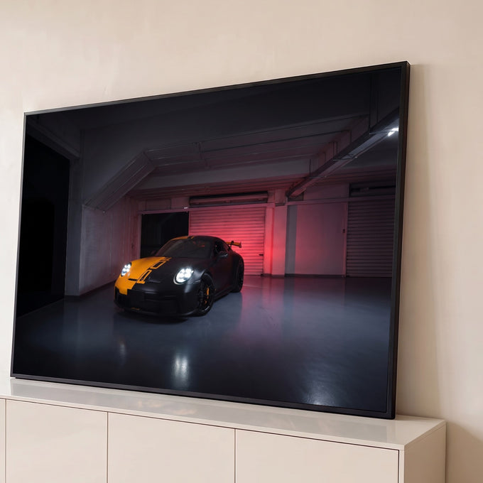 Porsche 911 GT3 preto fosco com faixa laranja e faróis acesos em garagem com luz vermelha, quadro decorativo
