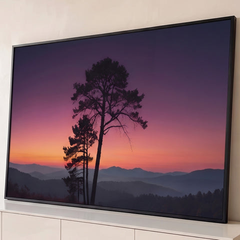 Pinheiros em silhueta sob céu roxo e laranja ao pôr do sol e montanhas enevoadas, quadro decorativo