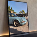 Porsche 911 vintage azul-claro com faixa laranja e rodas clássicas sob céu azul, quadro decorativo