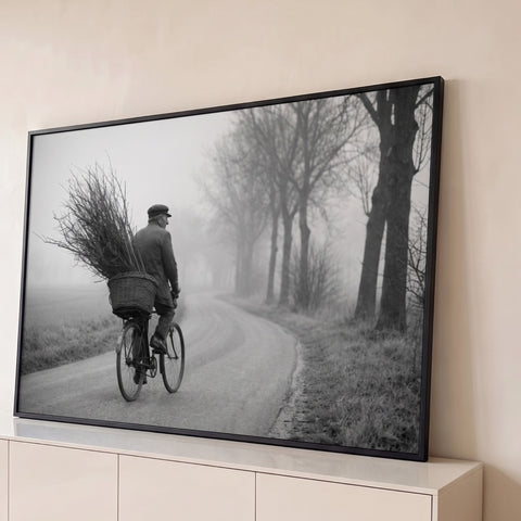 Senhor de bicicleta com cesto de galhos em estrada rural enevoada, foto preto e branco, quadro decorativo