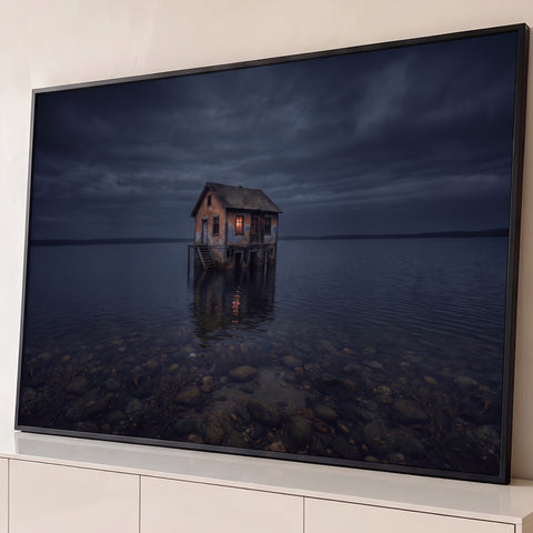 Casa sobre pilotis no lago à noite, janela acesa refletida na água e céu nublado, quadro decorativo