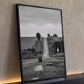 Menina de vestido xadrez caminhando em estrada rural sob céu nublado em preto e branco quadro decorativo