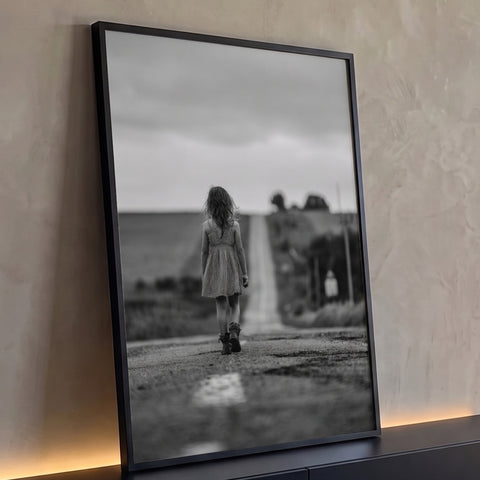 Menina de vestido xadrez caminhando em estrada rural sob céu nublado em preto e branco quadro decorativo