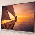 Quadro Decorativo Grande Mulher ao Pôr do Sol para Sala | quadros decorativos para sala | mulher sentada na proa de veleiro observando pôr do sol laranja e roxo sobre o mar | Porao dos Quadros