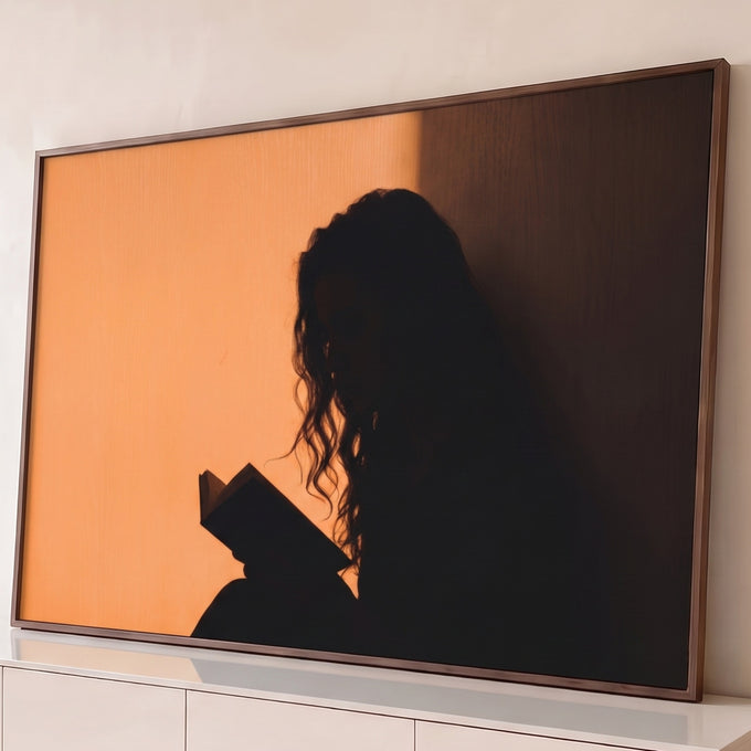 Silhueta de mulher de cabelos cacheados lendo livro em contraluz sobre parede laranja, quadro decorativo
