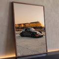 Porsche 911 preto rebaixado com trem amarelo desfocado ao fundo no pôr do sol, quadro decorativo