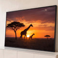 Girafa e filhote em silhueta na savana africana com acácia e sol se pondo em céu laranja, quadro decorativo