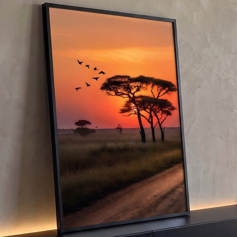 Pôr do sol laranja na savana com acácias em silhueta, pássaros voando e estrada de terra, quadro decorativo