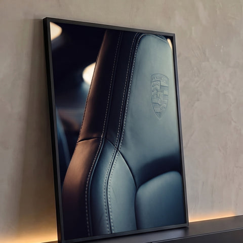 Close de banco Porsche em couro preto com costura branca e brasão em relevo, quadro decorativo
