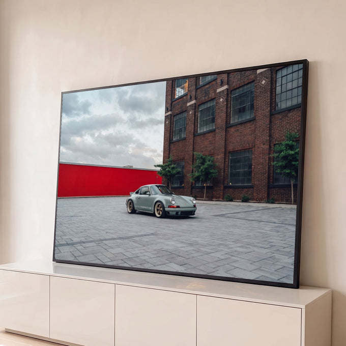 Porsche 911 verde sage em pátio de pedra diante de prédio de tijolos e muro vermelho, quadro decorativo