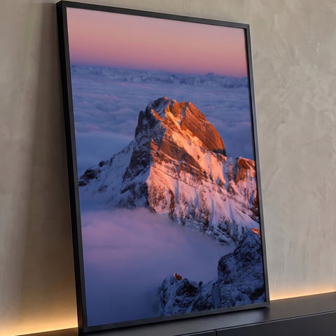 Pico de montanha nevada iluminado pelo sol sobre mar de nuvens e céu rosa, quadro decorativo
