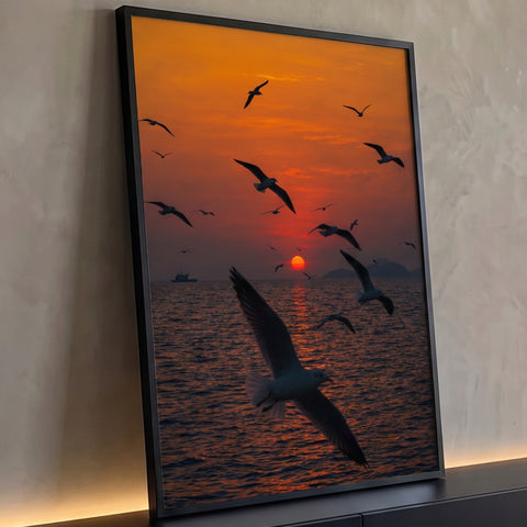 Gaivotas voando sobre o mar com sol vermelho no horizonte e céu laranja, quadro decorativo